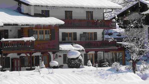 Un edificio de varios pisos con tejados y balcones cubiertos de nieve, que presenta una arquitectura tradicional con ventanas y puertas visibles.