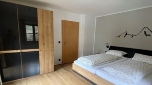 Un dormitorio con piso de madera, cama con ropa de cama blanca, armario de madera y pared con diseño de montaña.