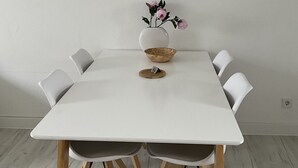 A white dining table with four chairs, a vase with pink flowers, and a decorative bowl on the table. - CITY FLAT Center Freudenstadt opposite Kurhaus  (Freudenstadt)