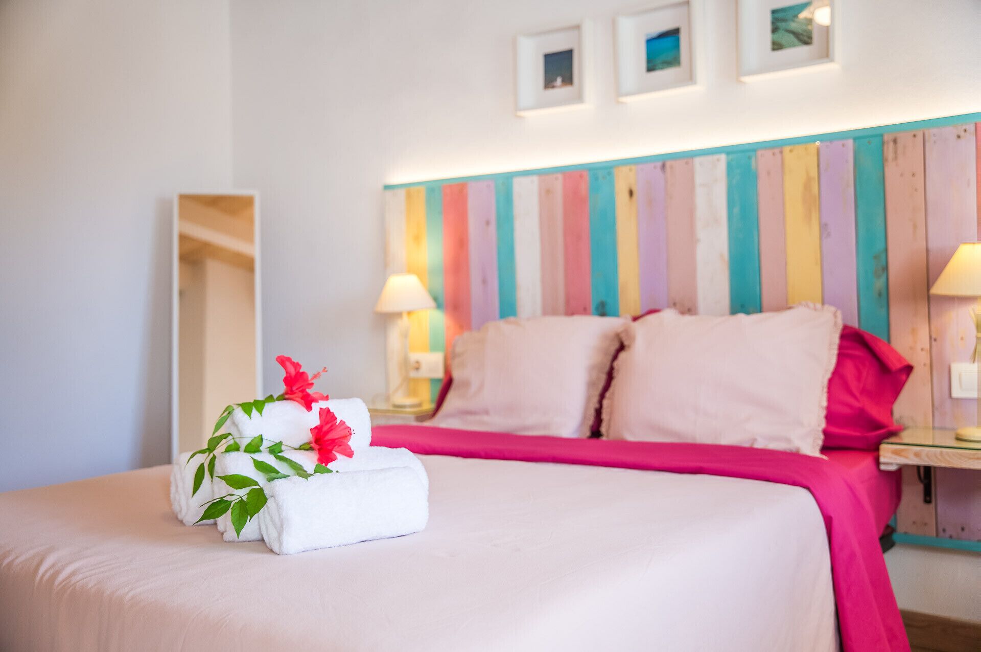 A hotel room with a bed, pillows, a nightstand, a lamp, and a colorful wall panel.
