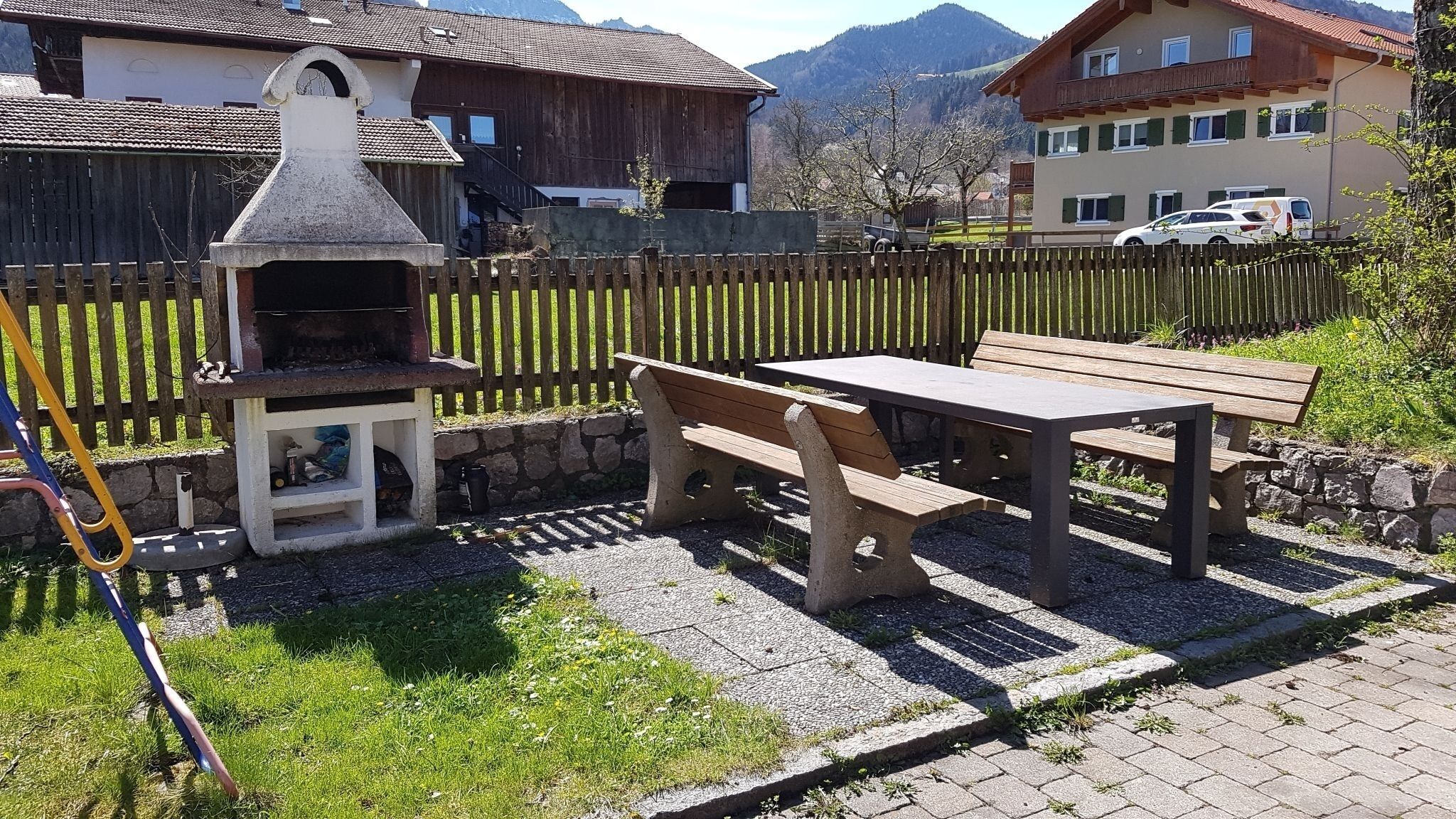 Eine Terrasse mit Grill, einem Holztisch und Bänken.