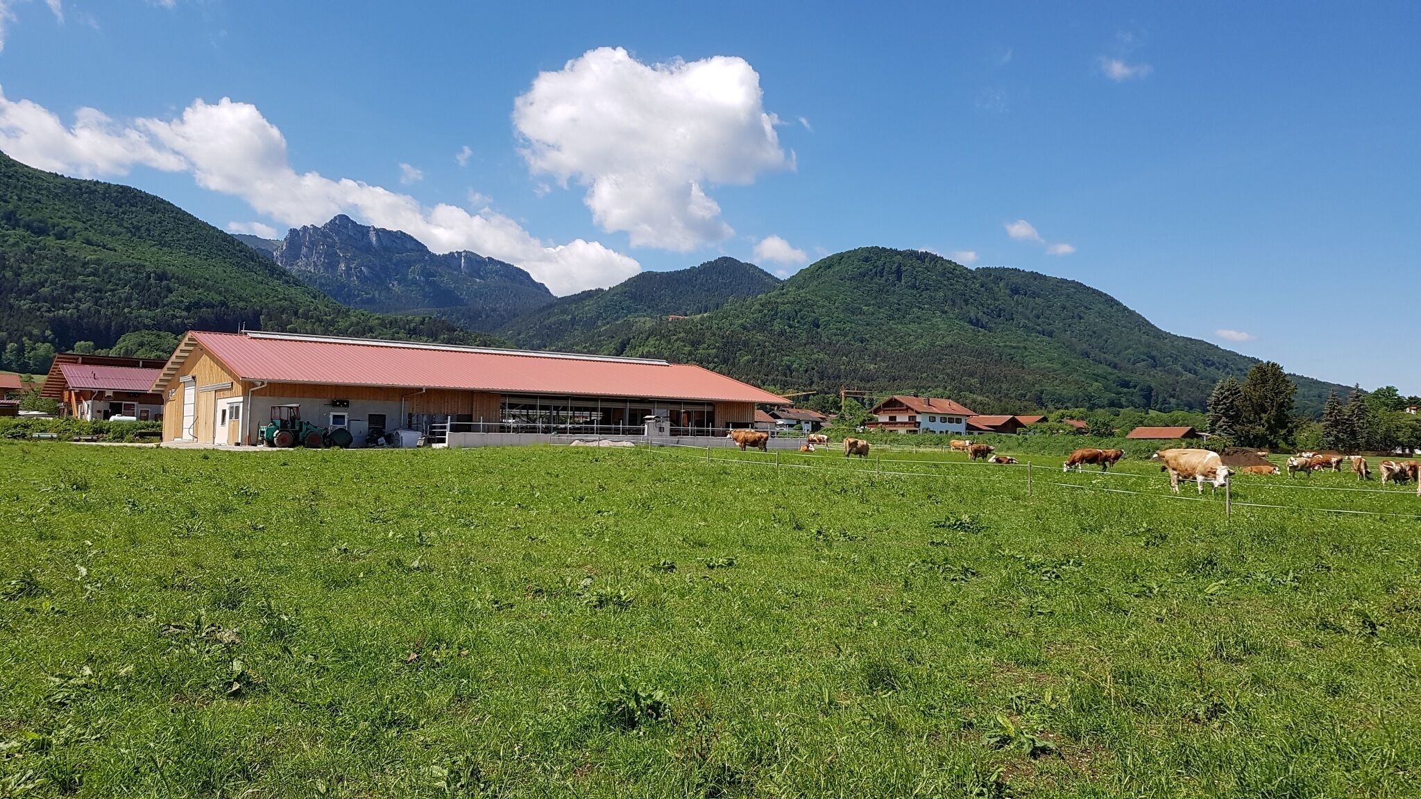 A rural farm with a large barn, green fields, and mountains in the background.