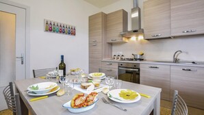 A modern kitchen with wooden cabinets, a stainless steel range hood, and a dining table set with plates, glasses, and a bottle of wine.