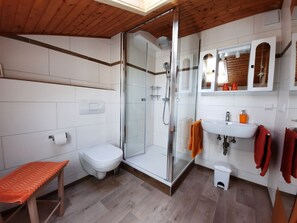 Ein modernes Badezimmer mit einer Duschkabine aus Glas, einer weißen Toilette, einer Sitzbank, einem Waschbecken mit Spiegel und Holzboden.
