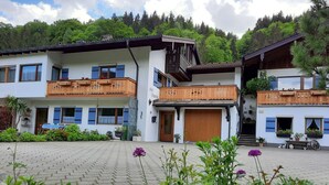 Ein traditionelles Chalet mit Holzbalkon, einem courtyard aus Ziegelsteinen und üppigem Grün im Hintergrund.