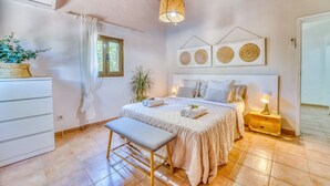 A bedroom with a bed, bedside table, bench, hanging light fixture, window, and wall art. - Finca Toni in Alcudia with pool close to the beach (Alcúdia)