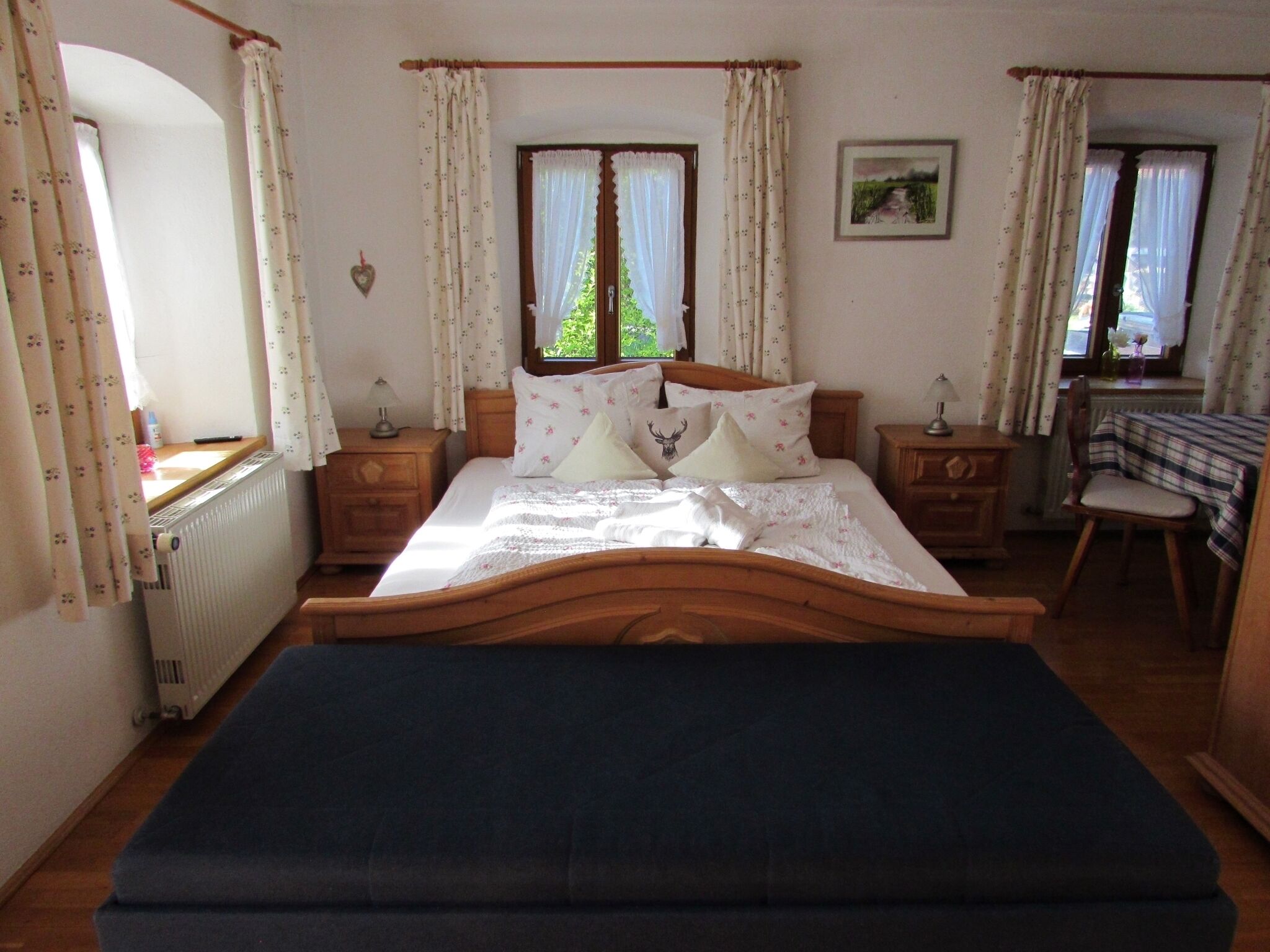 Ein Schlafzimmer mit einem hölzernen Bett, zwei Nachttischen, einem Sessel, einer Heizung und einem Fenster mit Vorhängen.