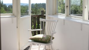 Una habitación con una mecedora cerca de la ventana, piso de madera y vista a plantas al exterior.