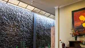 A dining area with a stone wall, wooden furniture, and a painting on the wall. - Helena Guest House (Malang)