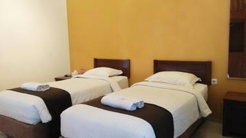 A hotel room with two single beds, each with a wooden headboard, white bedding, and a rolled towel on the bed.