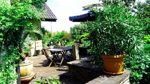 Eine Terrasse mit Ziegelwand, einem Holztisch und verschiedenen Blumentöpfen.