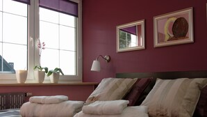 Ein Hotelzimmer mit großem Fenster, einem Bett mit gestreifter Bettwäsche, zwei Nachttischen mit Lampen und einem Kunstwerk an der Wand.