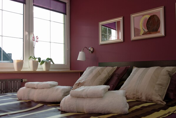 A hotel room with a large window, a bed with striped bedding, two bedside tables with lamps, and artwork on the wall.
