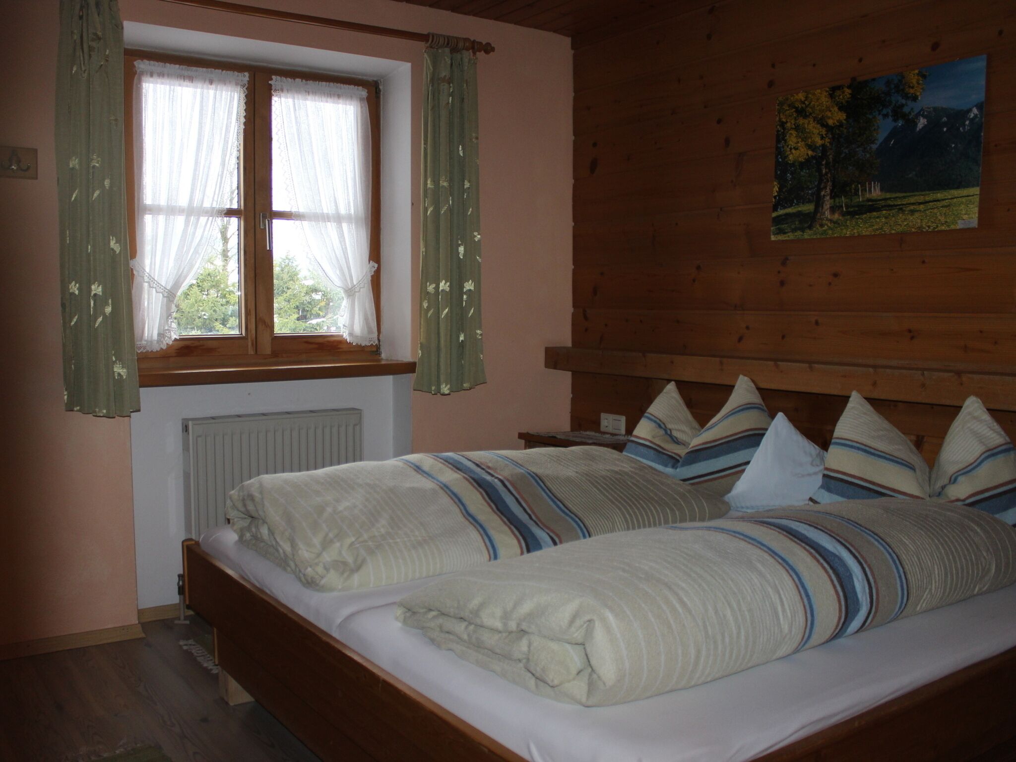 A bedroom with two beds, a window with curtains, a radiator, and a painting on the wall.