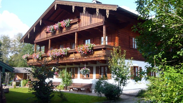Un bâtiment en bois doté d’un balcon, d’un banc et de plantes en pot.