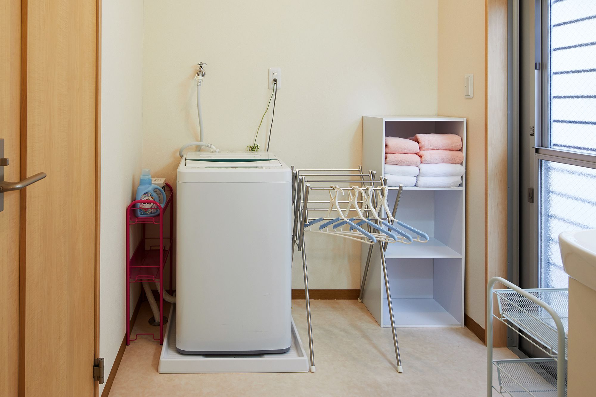 A laundry room with a washing machine, a drying rack, and shelves with folded towels.
