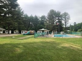 Un parque con un área de juegos, una piscina pequeña y un quiosco.
