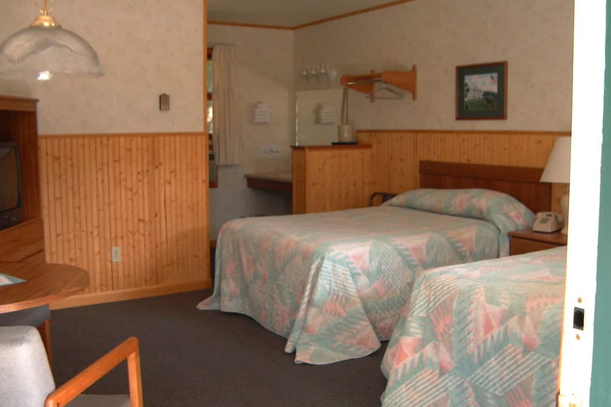 A hotel room with two beds, a desk, a chair, a television, a lamp, and a picture on the wall.