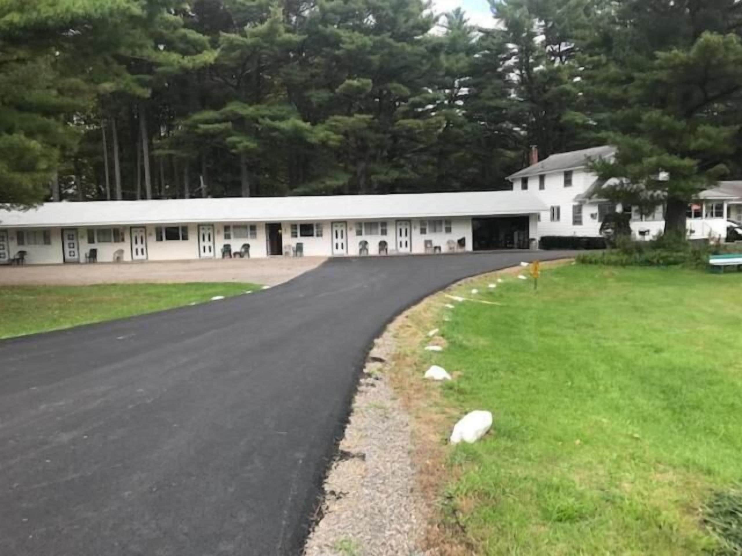 A motel with a long driveway leading to a row of rooms, surrounded by trees.