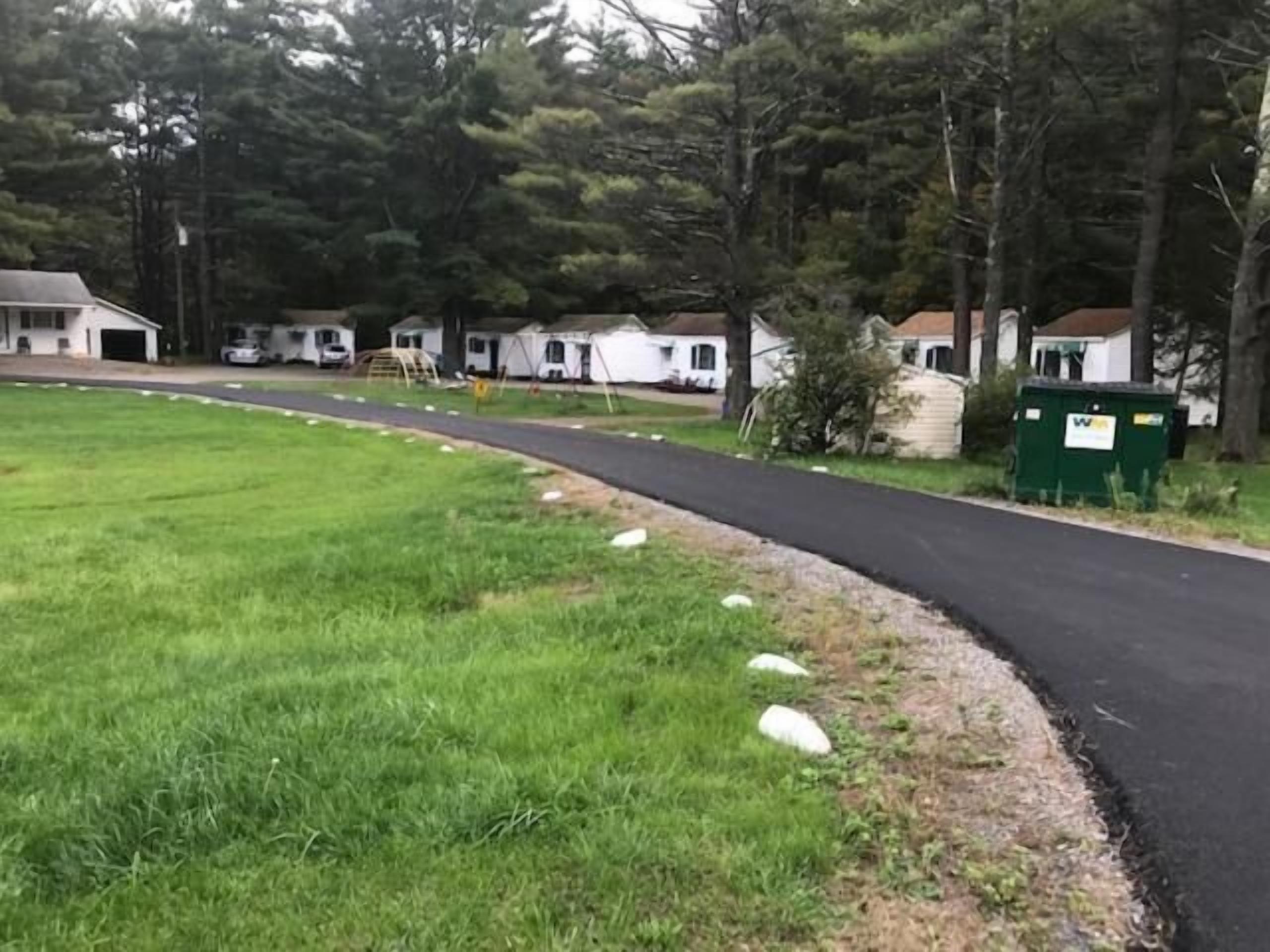 A residential area with a paved road, grassy areas, and mobile homes.