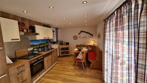 A compact kitchen with wooden cabinets, a built-in oven, and a dining area with a bench and chairs. - Ferienwohnung Nr. 1, 1-2 Personen, 60 qm, Dusche/WC, Terrasse, TV, W-LAN, 1 Schlafzimmer + 1 Wohnschlafzimmer, Kachelofen (Ramsau bei Berchtesgaden)