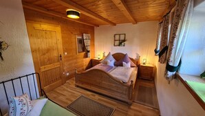 A cozy wooden bedroom with a bed, nightstands, and a window with curtains. - Ferienwohnung Nr. 1, 1-2 Personen, 60 qm, Dusche/WC, Terrasse, TV, W-LAN, 1 Schlafzimmer + 1 Wohnschlafzimmer, Kachelofen (Ramsau bei Berchtesgaden)