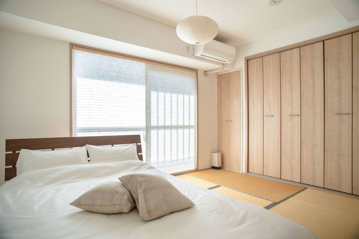 A bedroom with a large bed, a wardrobe, and a window with blinds.