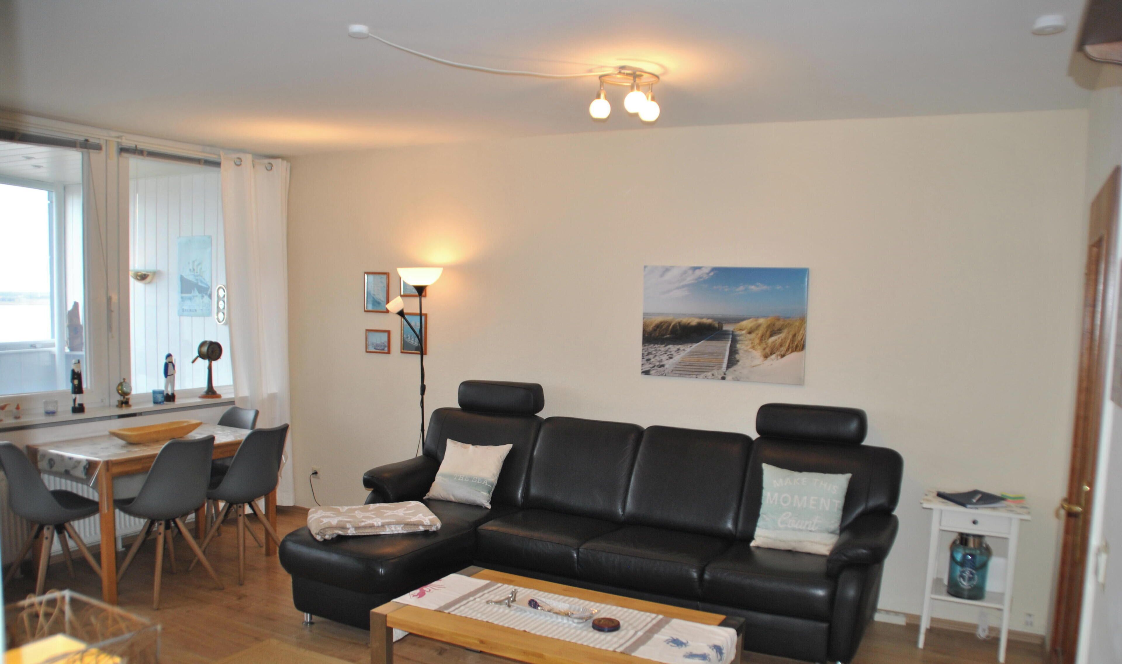 A modern living room with a black leather sofa, wooden coffee table, and a dining area with a table and chairs.