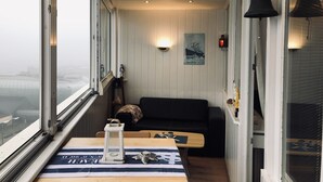 Un balcon étroit offrant une vue sur la ville, un canapé noir, une petite table avec une lanterne et une cloche fixée au mur.