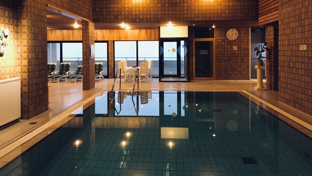 Une piscine intérieure avec vue sur la mer, des murs en bois et une horloge au mur.
