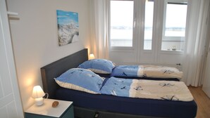 Une chambre à coucher avec un lit, une table de chevet avec une lampe, un tableau au mur et une fenêtre donnant sur un beau paysage.