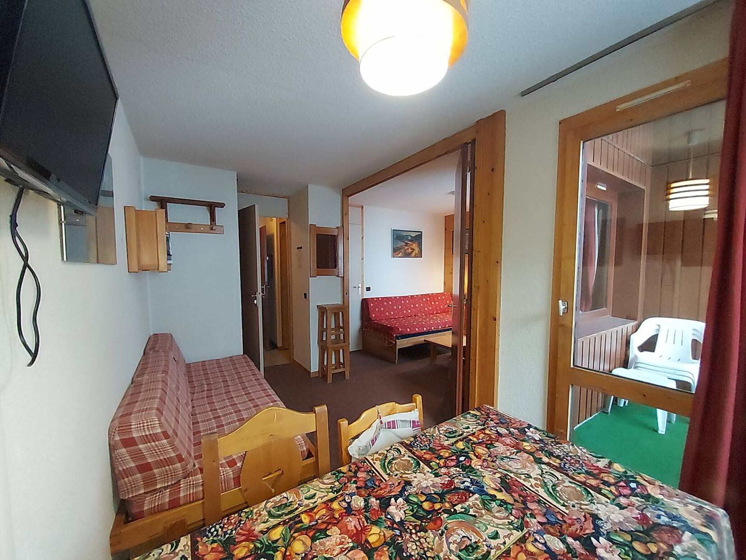 Una habitación pequeña y acogedora con una cama, una mesa de madera y una silla. Hay un espejo en la pared y una puerta que da a otra habitación.