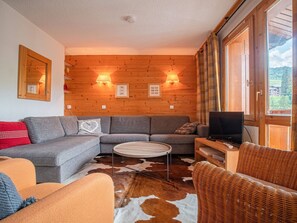 Una sala de estar acogedora con un muro de madera, un sofá, una mesa de centro y un sillón de mimbre.