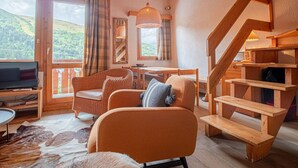 Un salon chaleureux avec un escalier en bois, un téléviseur et une vue sur l’extérieur.