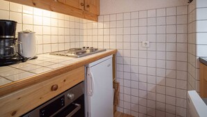 Une cuisine compacte avec des meubles en bois, un crédence carrelée de couleur blanche, une machine à café, une cuisinière et un petit réfrigérateur.