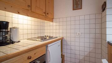 Une cuisine compacte avec des meubles en bois, un crédence carrelée de couleur blanche, une machine à café, une cuisinière et un petit réfrigérateur.