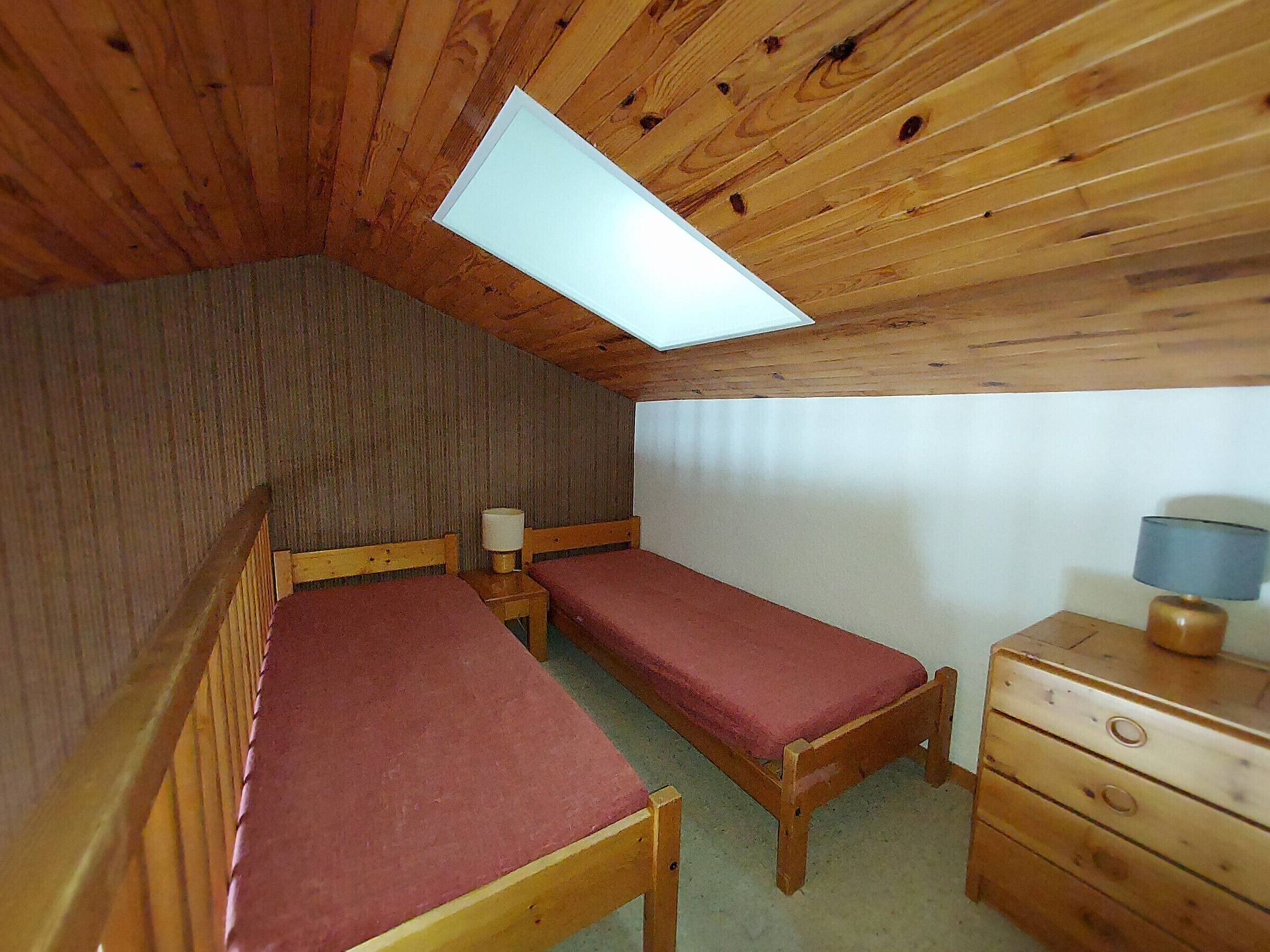 A small, cozy room with two wooden beds, a wooden dresser, and a skylight.