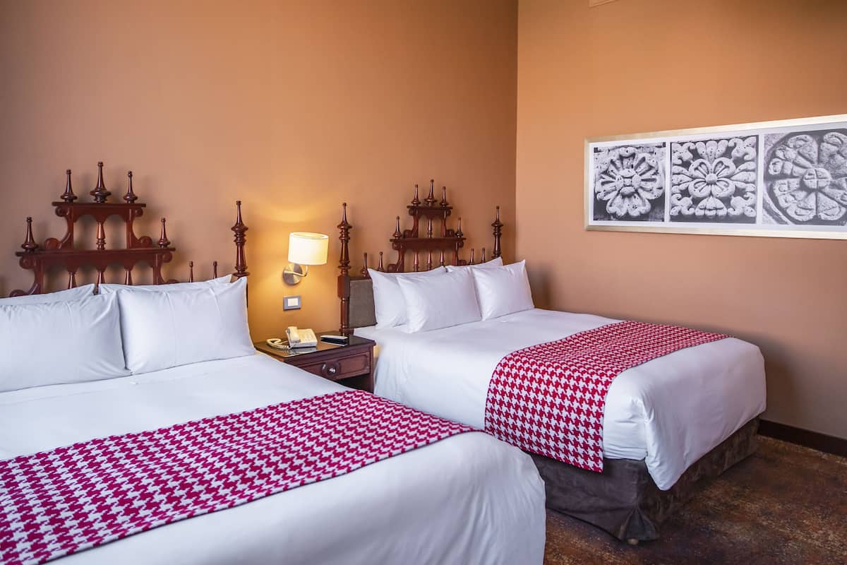 Une chambre d’hôtel avec deux lits, un lustre, une table de chevet et un mur orné de panneaux décoratifs.