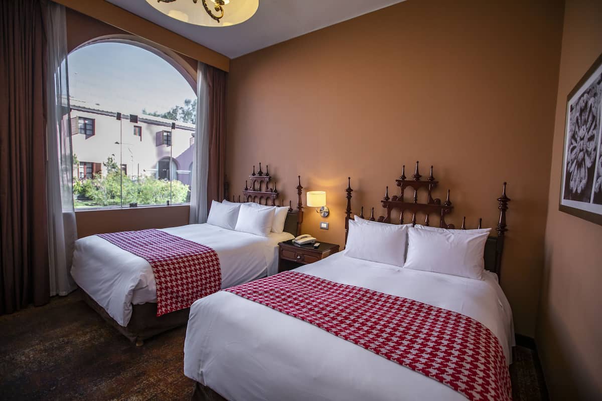 Une chambre d’hôtel avec deux lits, une grande fenêtre et une table de chevet avec une lampe.