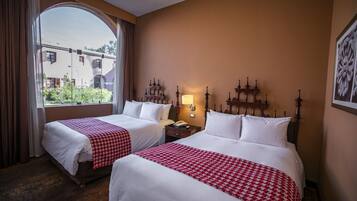 Een hotelkamer met twee bedden, een groot raam en een nachtkastje met een lamp.