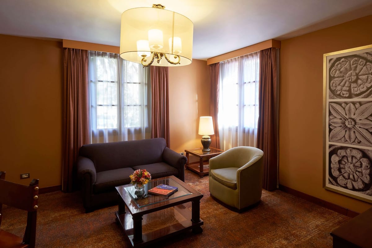 Une chambre d’hôtel équipée d’un canapé, d’un fauteuil, d’une table basse, d’une lampe et d’une œuvre d’art au mur.