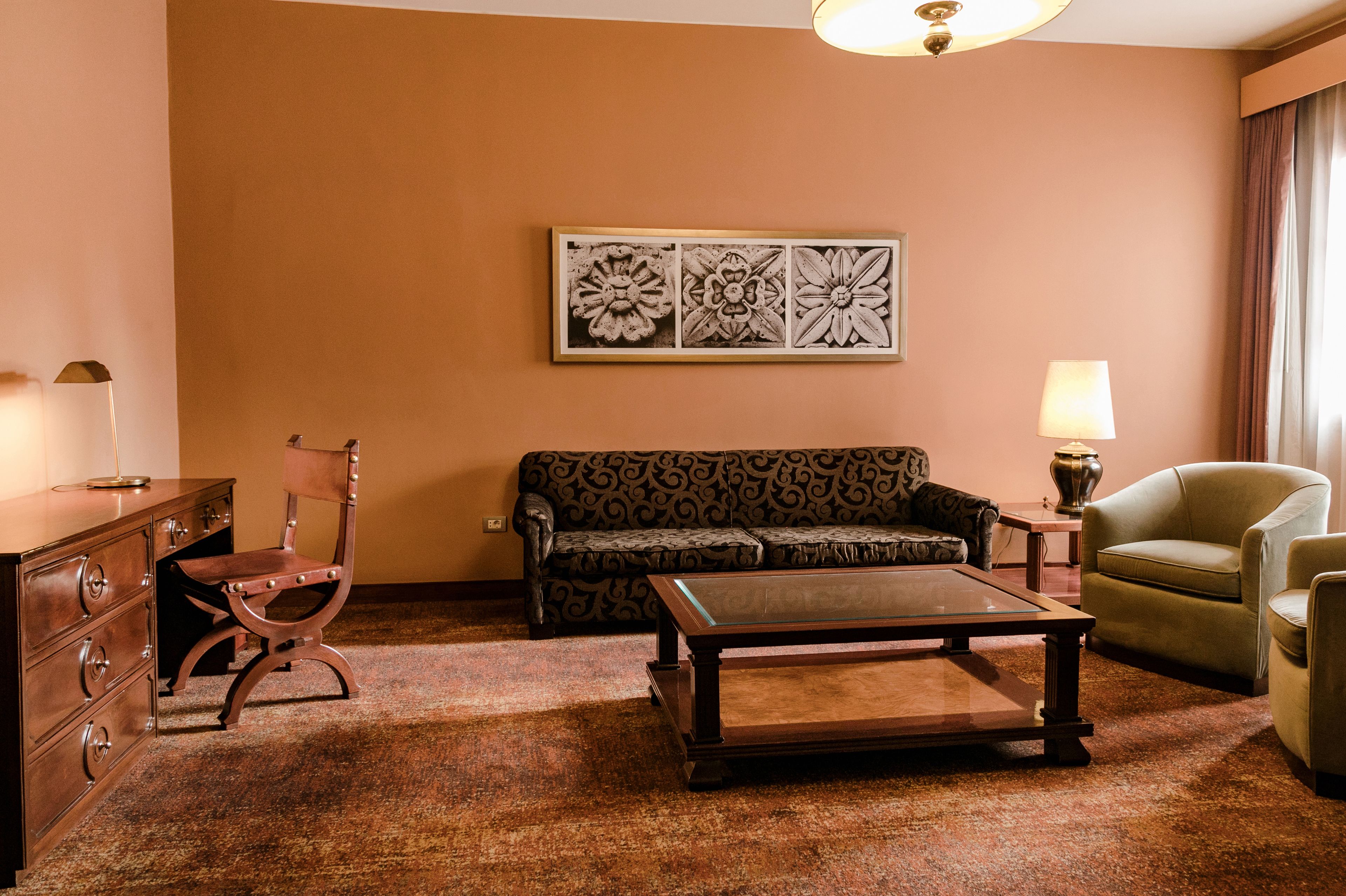 Una sala de estar con un sofá estampado, una mesa de centro de madera, un sillón verde, una silla de madera y una obra de arte colgada en la pared.