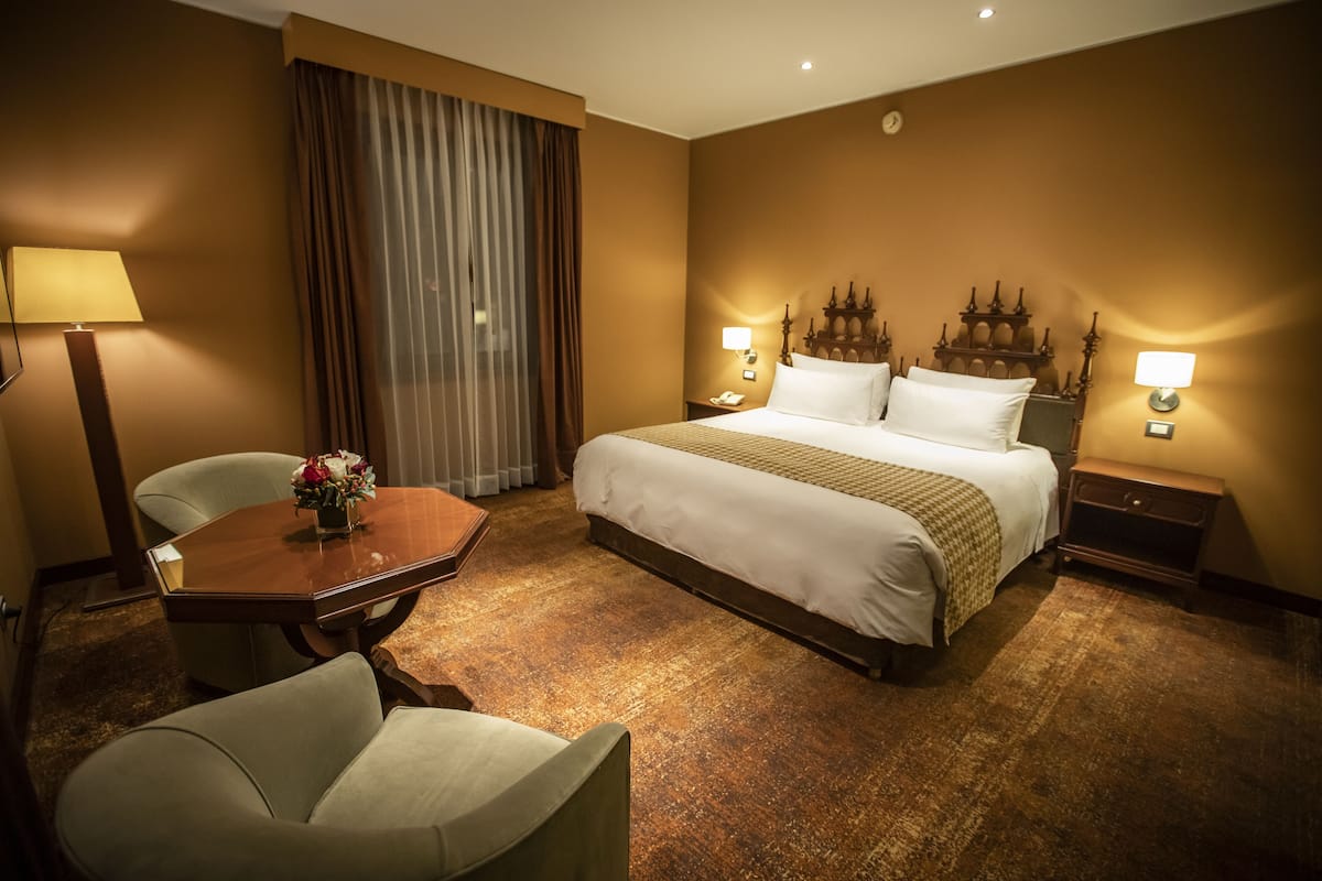 Une chambre d’hôtel avec un grand lit, deux tables de chevet, un bureau avec une chaise et une fenêtre avec des rideaux.