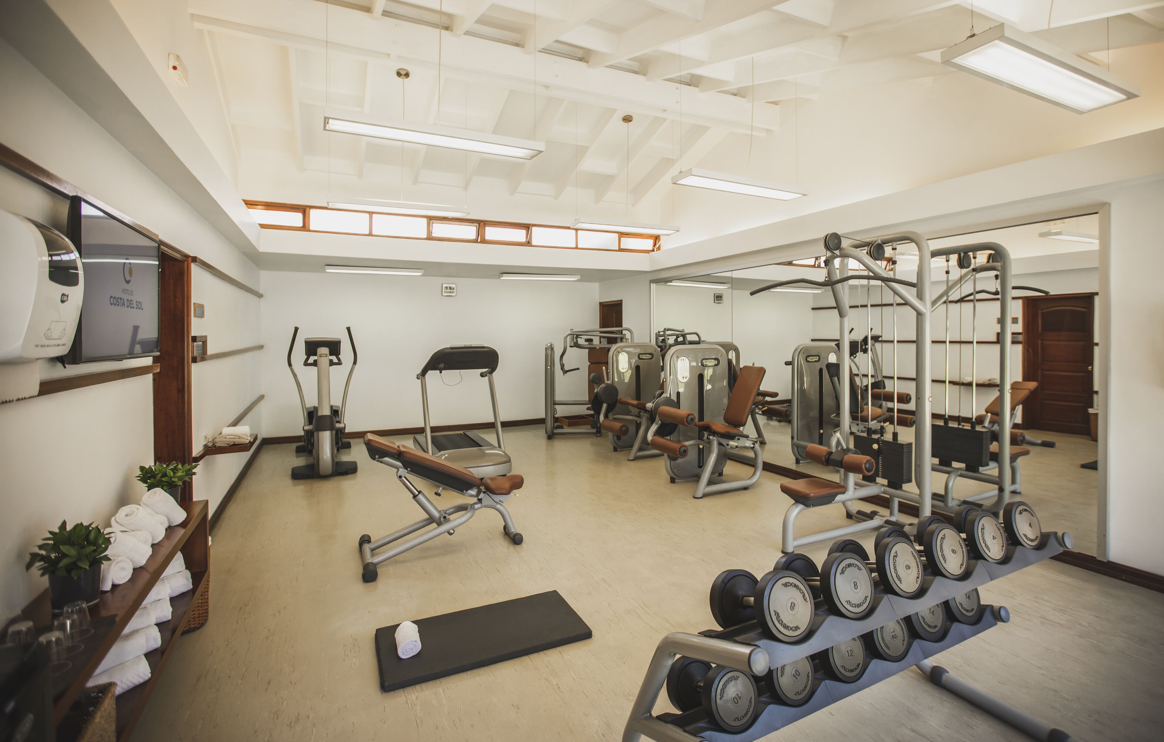 Un gimnasio con varios equipos de ejercicio, una colchoneta negra y un estante con mancuernas.