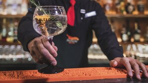 Un barman tient un verre contenant une boisson appelée « BULLDOG » dans un bar. On aperçoit un comptoir et des bouteilles en arrière-plan.