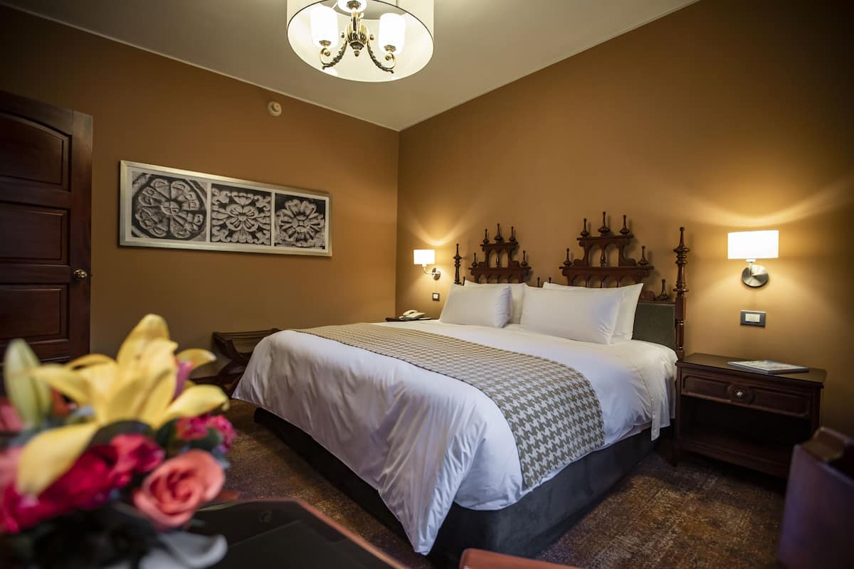 Une chambre d’hôtel avec un grand lit, une table de chevet, une lampe et une œuvre d’art accrochée au mur.