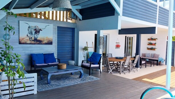 Un espace extérieur abrité, aménagé avec une table à manger, des chaises et un canapé bleu.