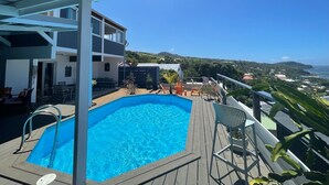 Un espace piscine doté d’une terrasse en bois, d’un escalier métallique pour accéder à la piscine et de sièges d’extérieur.