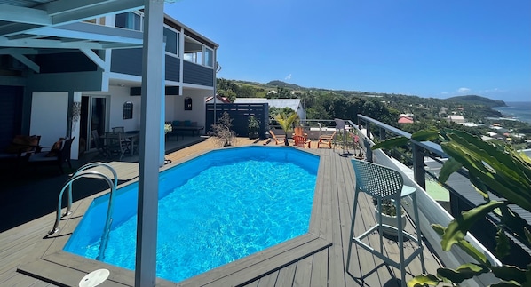 A pool area with a wooden deck, a metal pool ladder, and outdoor seating. - Villa with beautiful sea view and pool (saint pierre)