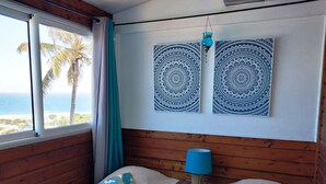 Une chambre avec deux lits, une fenêtre donnant sur l’océan et deux éléments de décoration murale bleus à motifs.